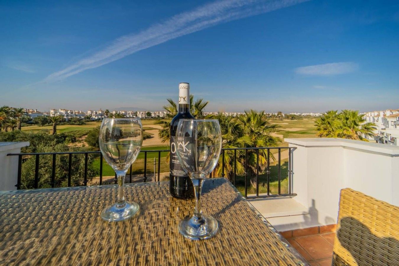 A balcony with a table, two wine glasses, and a bottle of wine.