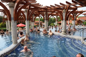 Ein großer Außenpool mit mehreren Personen, die das Wasser genießen, umgeben von Holzbalkonen und Säulen.