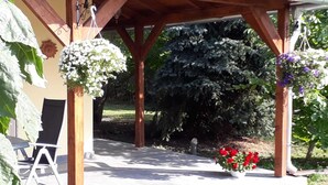 A covered outdoor seating area with a pergola, a chair, and a potted plant with red flowers.