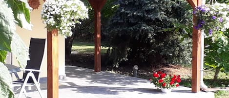 A covered outdoor seating area with a pergola, a chair, and a potted plant with red flowers.
