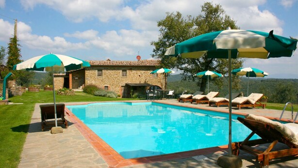 Ein Poolbereich mit Liegestühlen und Sonnenschirmen, ein Steinhaus und ein Blick auf die umliegende Landschaft.