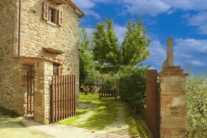 A stone building with a wooden gate, a paved path, and a tall structure with inscriptions. - Fully detached and fenced stone cottage with an outside porch. Garden equipped with table, chairs, d (Castiglion Fiorentino)
