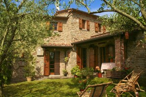 A stone house with a covered porch, wooden shutters, and potted plants.