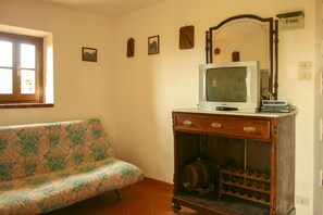 A room with a sofa, a television on a wooden cabinet, a wine rack, and a window.