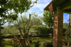 A garden with a brick column, wooden chairs, and potted plants.
