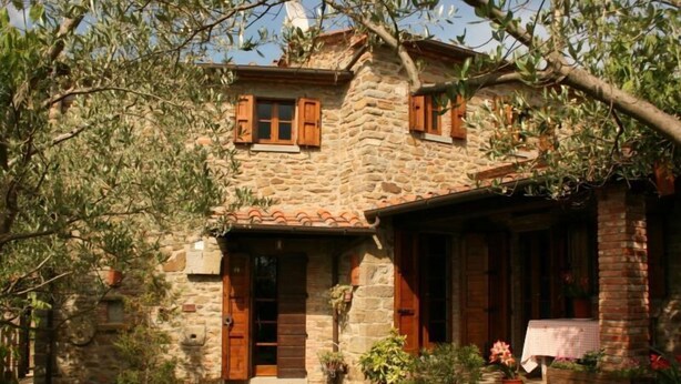 Ein Haus aus Stein mit hölzernen Fensterläden, einem Ziegeldach und einer kleinen Veranda mit Blumentöpfen.