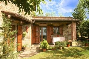 A rustic stone house with wooden shutters, a covered porch, and a garden with potted plants. - Fully detached and fenced stone cottage with an outside porch. Garden equipped with table, chairs, d (Castiglion Fiorentino)