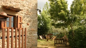 Ein Steinhaus mit Holzpforte, ein Garten mit Bäumen und Gartenmöbeln.