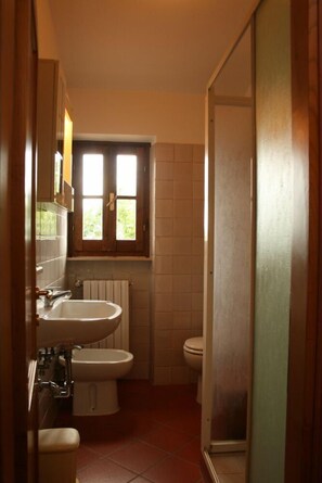 A compact bathroom with a sink, toilet, and bidet. There is a window above the sink allowing natural light.