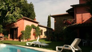 Una piscina con sillones de descanso, un edificio de piedra y follaje.