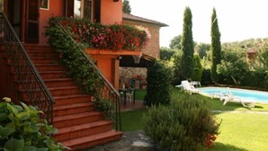 Una casa con una escalera que lleva a un balcón con flores, piscina y jardín.