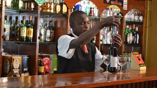 A bartender pouring a drink at a bar with shelves of liquor bottles in the background. - Batian Grand Hotel (Nyeri)