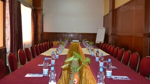 A conference room with a long table set for a meeting, red chairs, water bottles, and a projector screen. - Batian Grand Hotel (Nyeri)
