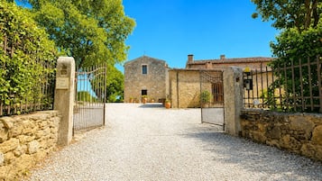 Un bâtiment en pierre avec une allée gravillonnée et des portails en métal.