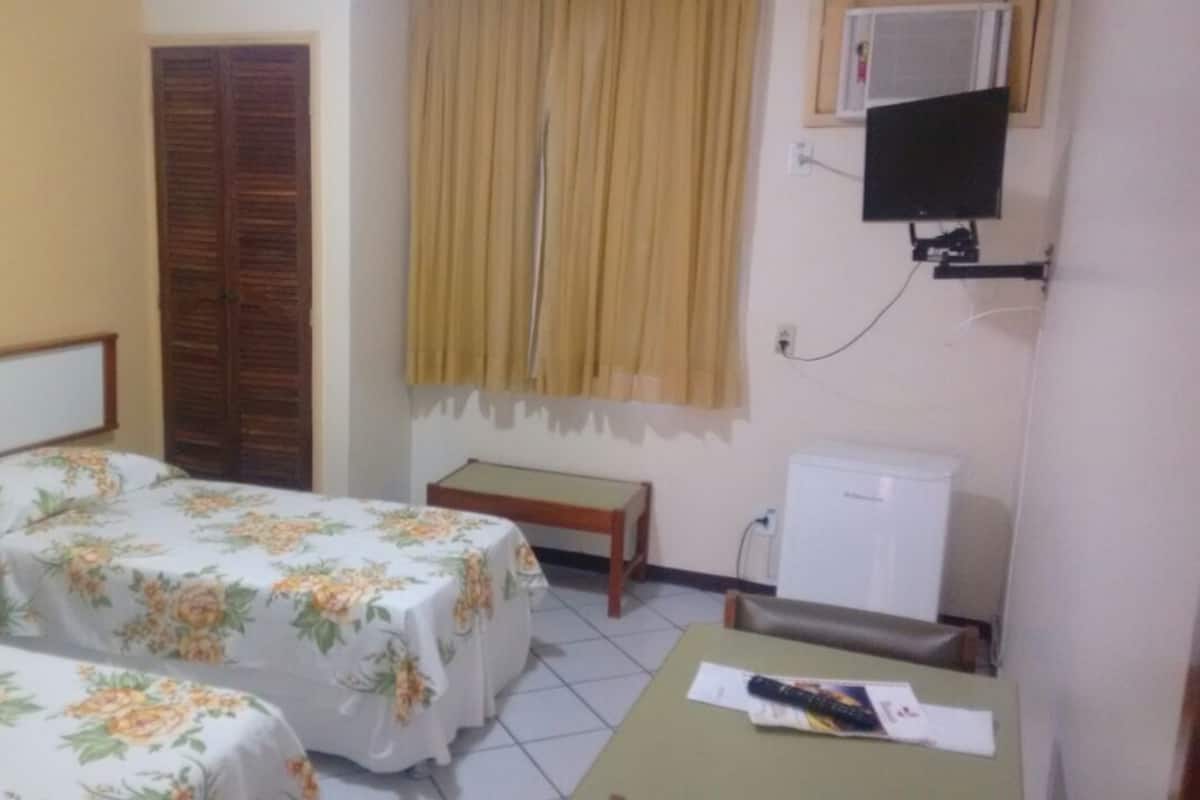 Habitación de hotel con dos camas, una mesita, un banco, un televisor y un radiador.