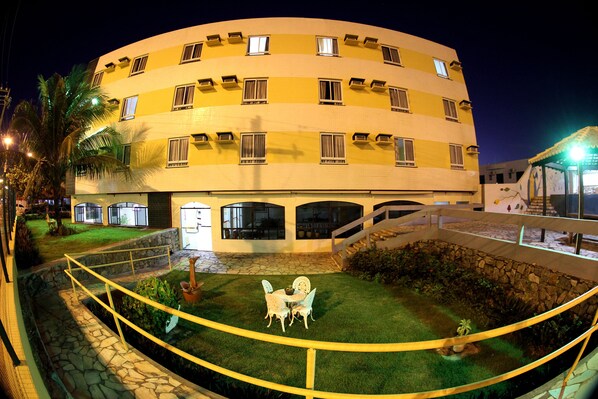 Un hotel de varios pisos con fachada curva, zona de estar al aire libre y césped bien cuidado.