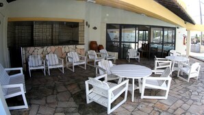 Un patio exterior con sillas y mesas Adirondack blancas, piso de piedra y una zona de cocina con salpicadero de azulejos.