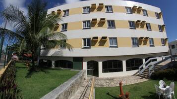 A multi-story hotel with a curved facade, balconies, and a central courtyard with a palm tree and seating area.