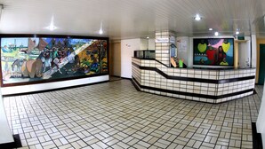 Zona de recepción con suelos de baldosas, un mostrador de recepción y un gran mural que representa una escena histórica.