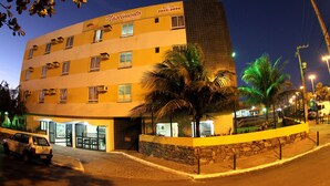 Un hotel de varios pisos con fachada de piedra, múltiples balcones y una palmera en primer plano.