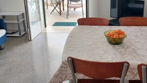 Un coin repas avec une table dressée pour deux personnes, un saladier de fruits et un téléviseur fixé au mur.