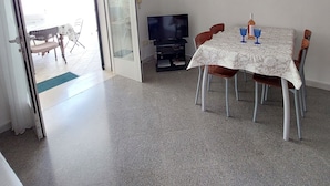 Un coin repas avec une table dressée pour deux personnes, un téléviseur et une porte donnant sur un espace extérieur.