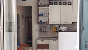 Une cuisine de taille réduite avec des meubles blancs, une horloge au mur et un coin repas comprenant une table et des chaises.