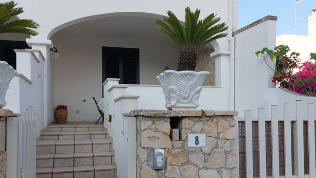 Un bâtiment blanc avec une entrée surmontée d’un mur en pierre, un panneau portant le chiffre 8 et un petit escalier menant à une porte.