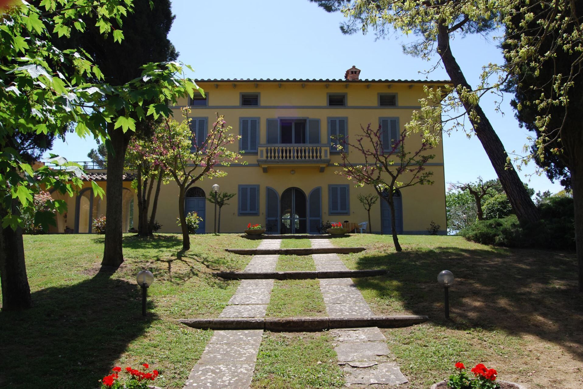 A yellow building with a central entrance, surrounded by a well-maintained garden and trees.