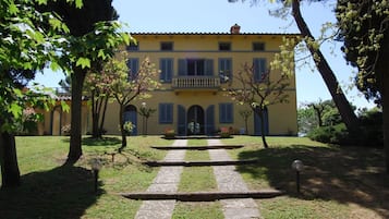A yellow building with a central entrance, surrounded by a well-maintained garden and trees.