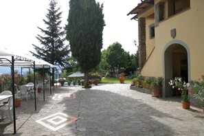 A courtyard with stone flooring, outdoor seating, potted plants, and a building with an arched entrance.