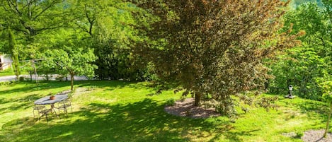 Jardim bem cuidado com uma mesa e cadeiras de jantar, rodeado por vegetação exuberante e árvores.