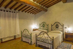 Una camera da letto con due letti, soffitto in legno, pavimento in pietra e un comodino con una lampada.