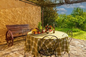 Zona pranzo all'aperto con tavolo apparecchiato per due, circondata da un muro in pietra e una panchina.