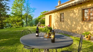 Zona pranzo all'aperto con un tavolo rotondo, due bottiglie di vino e una pianta in vaso.