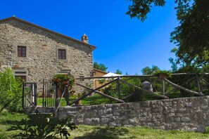 Un bâtiment en pierre à l’architecture traditionnelle, une clôture en bois et un ciel d’un bleu éclatant.