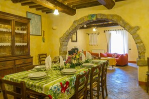 Un coin repas avec une table dressée pour quatre personnes, un buffet en bois doté de portes en verre et une arche en pierre menant à un salon.