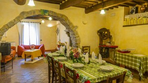 Zona pranzo con arco in pietra, travi in legno e tovaglia a quadri.