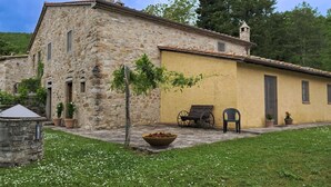 Un edificio in pietra con facciata gialla, un piccolo giardino con una panchina in legno e una carriola.