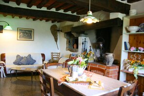 A rustic dining area with a wooden table set for a meal, surrounded by chairs. A brick oven is visible in the background, suggesting a kitchen or cooking area. - Stone farmhouse with private swimming pool, hilly, panoramic and quiet position, surrounded by silve (Cortona)