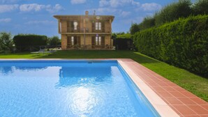 A swimming pool with a brick border, a large brick building with a balcony in the background, and a well-maintained hedge to the right. - Typical Valdichiana farmhouse in red bricks, near the border between Tuscany and Umbria and a few km (Montepulciano)