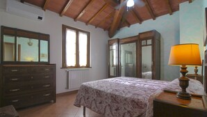 A bedroom with a bed, a dresser, a lamp, a window, and a radiator. - Typical Valdichiana farmhouse in red bricks, near the border between Tuscany and Umbria and a few km (Montepulciano)