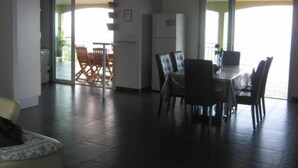 A spacious living area with a dining table and chairs, a refrigerator, and a sliding glass door leading to an outdoor area.