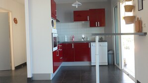 A modern kitchen with red cabinets, white appliances, and a large window providing natural light.