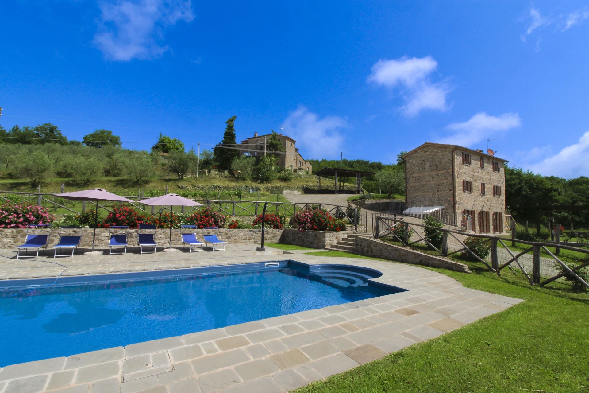 A swimming pool with lounge chairs and umbrellas, surrounded by stone walls and greenery.