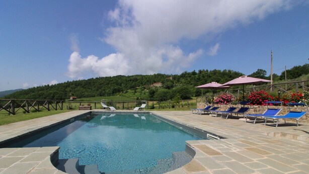 Une piscine rectangulaire bordée d’une terrasse en pierre, entourée de chaises longues et de parasols.