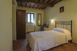 Quarto com cama, mesa de cabeceira, ventoinha, janela e porta.