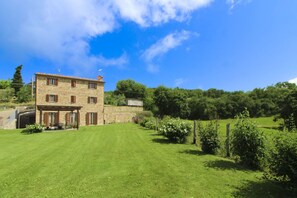 Un bâtiment en pierre avec une grande pelouse devant, entouré d’arbres et de verdure.