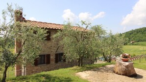 Une maison en pierre avec un toit de tuiles, entourée d’oliviers et d’une pelouse.