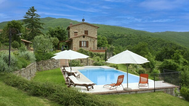 Ein Steinhaus mit Pool, umgeben von üppigem Grün und Hügeln.